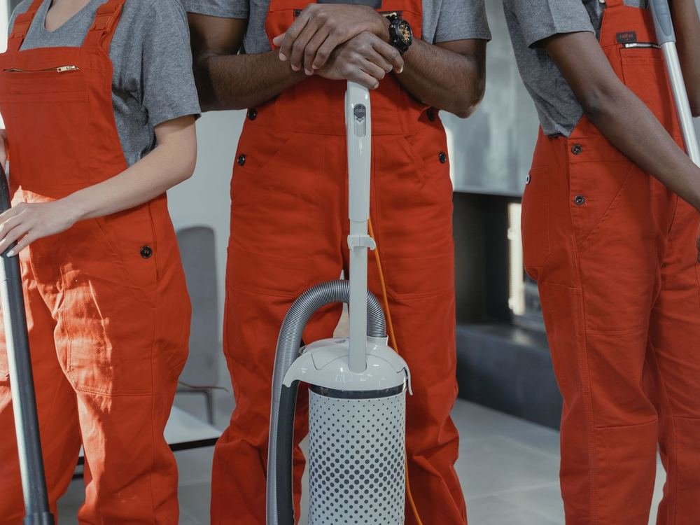 Cleaning team in orange overalls standing together around an upright vacuum cleaner