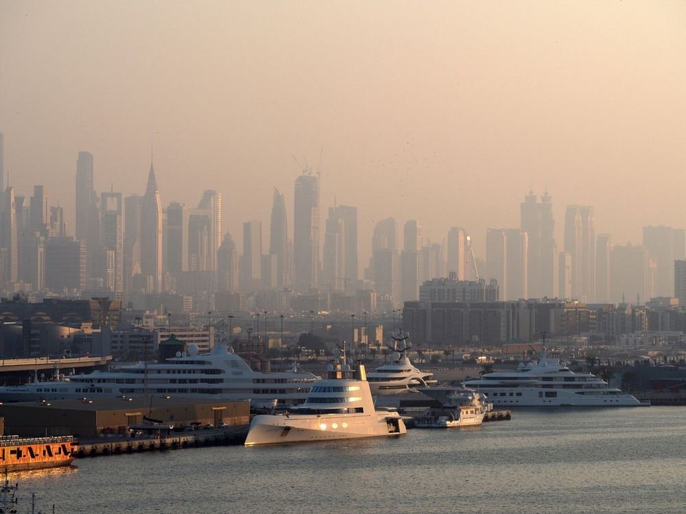 Hazy Dubai skyline seen across the water, with yachts moored in the foreground