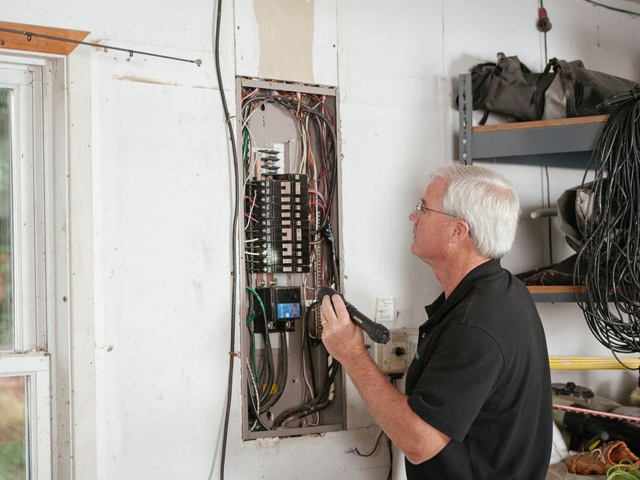 Electrician inspecting a wall-mounted electrical panel with a flashlight