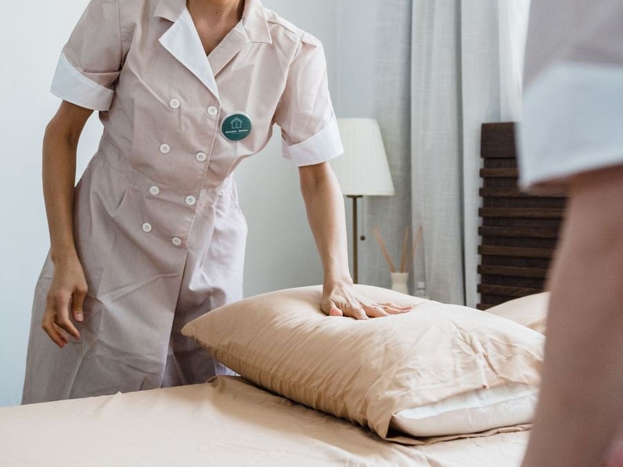 Housekeeper in a uniform smoothing a pillow while making a bed