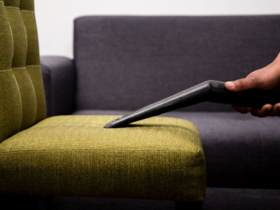 Vacuum nozzle cleaning the seat of an olive-green upholstered chair beside a grey sofa
